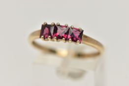 A 9CT GOLD THREE STONE RING, three square cut garnets, each claw set, to a polished yellow gold