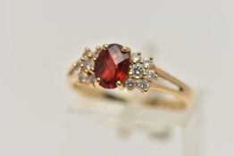 A YELLOW METAL GARNET AND DIAMOND RING, centring on an oval cut garnet four claw set, flanked with