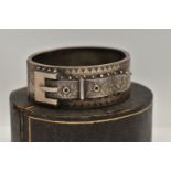 A LATE VICTORIAN SILVER HINGED BANGLE, of a belt and buckle design, floral detail with applied