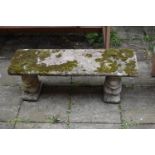 A WEATHERED COMPOSITE GARDEN BENCH, with a rectangular top, resting on twin pedestals depicting