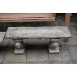 A WEATHERED COMPOSITE GARDEN BENCH, with a rectangular top, resting on twin pedestals depicting