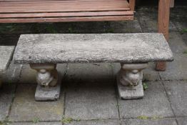 A WEATHERED COMPOSITE GARDEN BENCH, with a rectangular top, resting on twin pedestals depicting