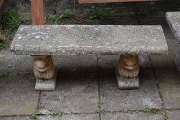 A WEATHERED COMPOSITE GARDEN BENCH, with a rectangular top, resting on twin pedestals depicting