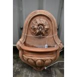 A TERRACOTTA WALL MOUNTED WATER FEATURE, with foliate detail surrounding the spout, which pours into
