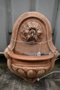 A TERRACOTTA WALL MOUNTED WATER FEATURE, with foliate detail surrounding the spout, which pours into
