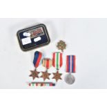 A TIN CONTAINING FOUR WWII MEDALS, a ribbon bar and a cap badge, the medals are all un-named and