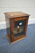 AN EARLY 20TH CENTURY OAK SMOKERS CABINET, with a glazed door enclosing two drawers, width 28cm x