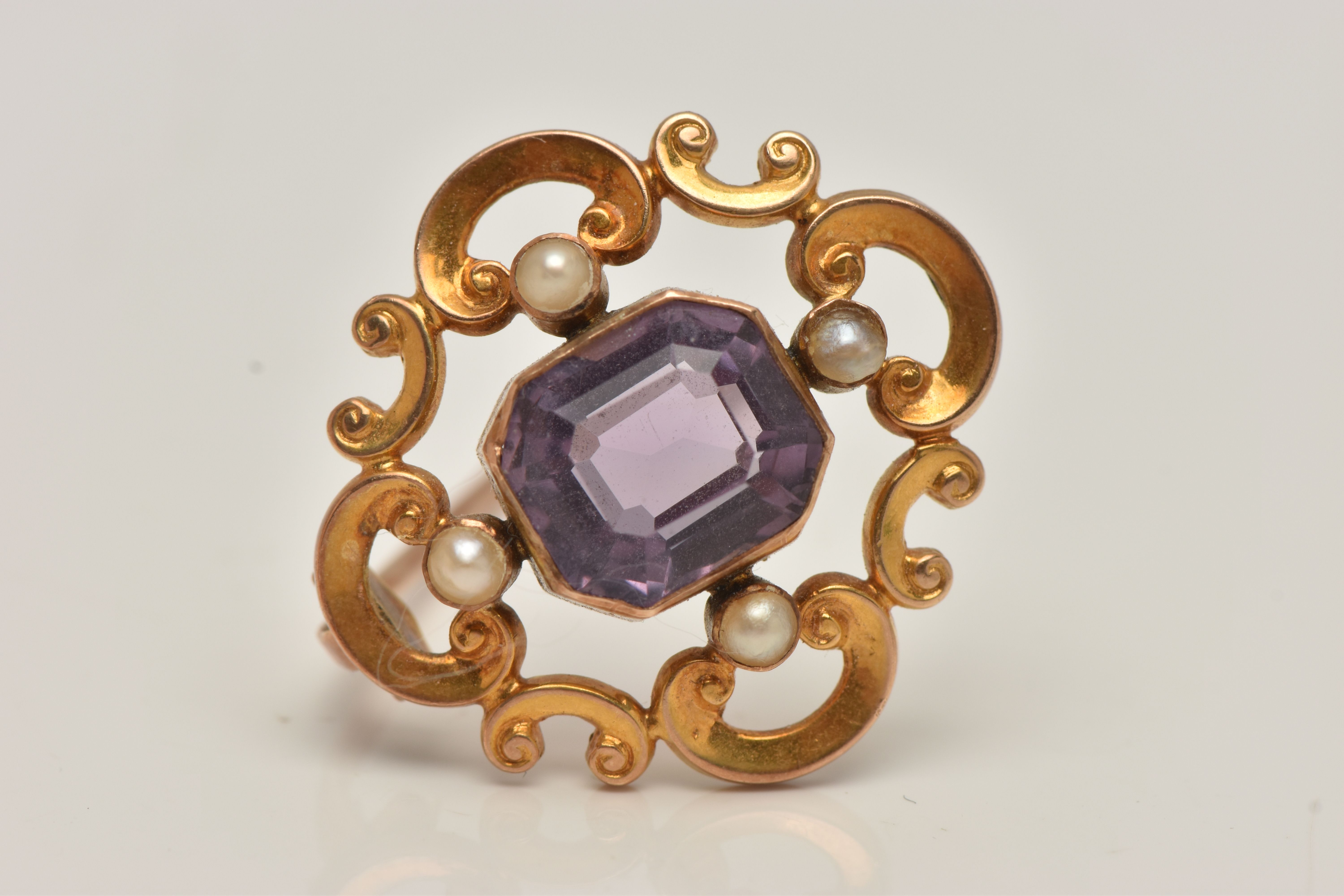 A YELLOW METAL AMETHYST AND SEED PEARL BROOCH, open work scrolling brooch set with a central emerald