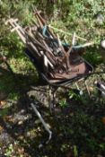 A WHEELBARROW CONTAINING VARIOUS GARDEN TOOLS, to include rakes, shovels, pitch forks, etc (