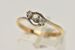 A YELLOW METAL THREE STONE DIAMOND RING, of a cross over design, set with a central round