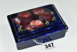 A MOORCROFT POTTERY RECTANGULAR LIDDED TRINKET BOX, 'Anemone' pattern on a dark blue ground, paper