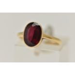 A YELLOW METAL GARNET RING, set with an oval cut garnet, collet set to a polished band, stamped