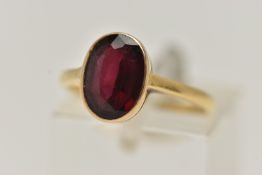 A YELLOW METAL GARNET RING, set with an oval cut garnet, collet set to a polished band, stamped