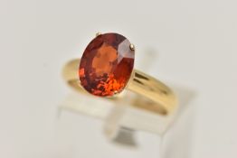 A GEM SET RING, oval cut orange stone, assessed as spessartine garnet, prong set in yellow metal,