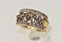 A 9CT GOLD GEM SET RING, designed as a wide band with three central flowers set with purple cubic