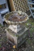 A WEATHERED COMPOSITE SHELL SHAPED BIRD BATH, on a square plinth, diameter 53cm x height 70cm (