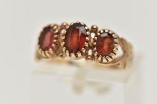 A 9CT GOLD GARNET RING, designed as three graduated oval garnets in claw settings to the scrolling