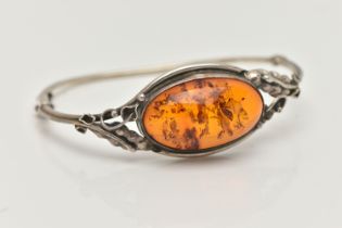 A SILVER AMBER BANGLE, designed as an oval cabochon of heated amber within a collet mount to the