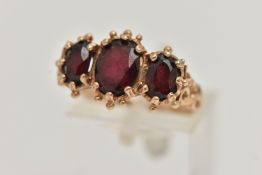 A 9CT GOLD THREE STONE RING, claw set with three oval cut garnets, applied bead work surround,