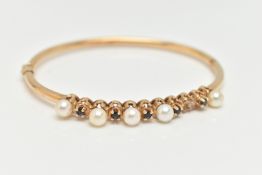 A 9CT GOLD GEM SET BANGLE, designed with a row of five cultured pearls (one pearl is missing),