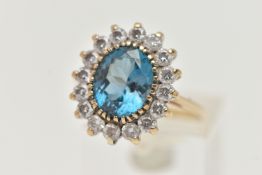 A 9CT GOLD CLUSTER RING, centring on an oval cut blue topaz, in a surround of colourless cubic