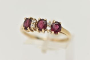A 9CT GOLD GARNET AND DIAMOND RING, with three oval cut garnets, each four claw set, interspaced