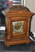 AN EARLY 20TH CENTURY WALNUT CASED CHIMING BRACKET CLOCK, the caddy hood with foliate carved detail,