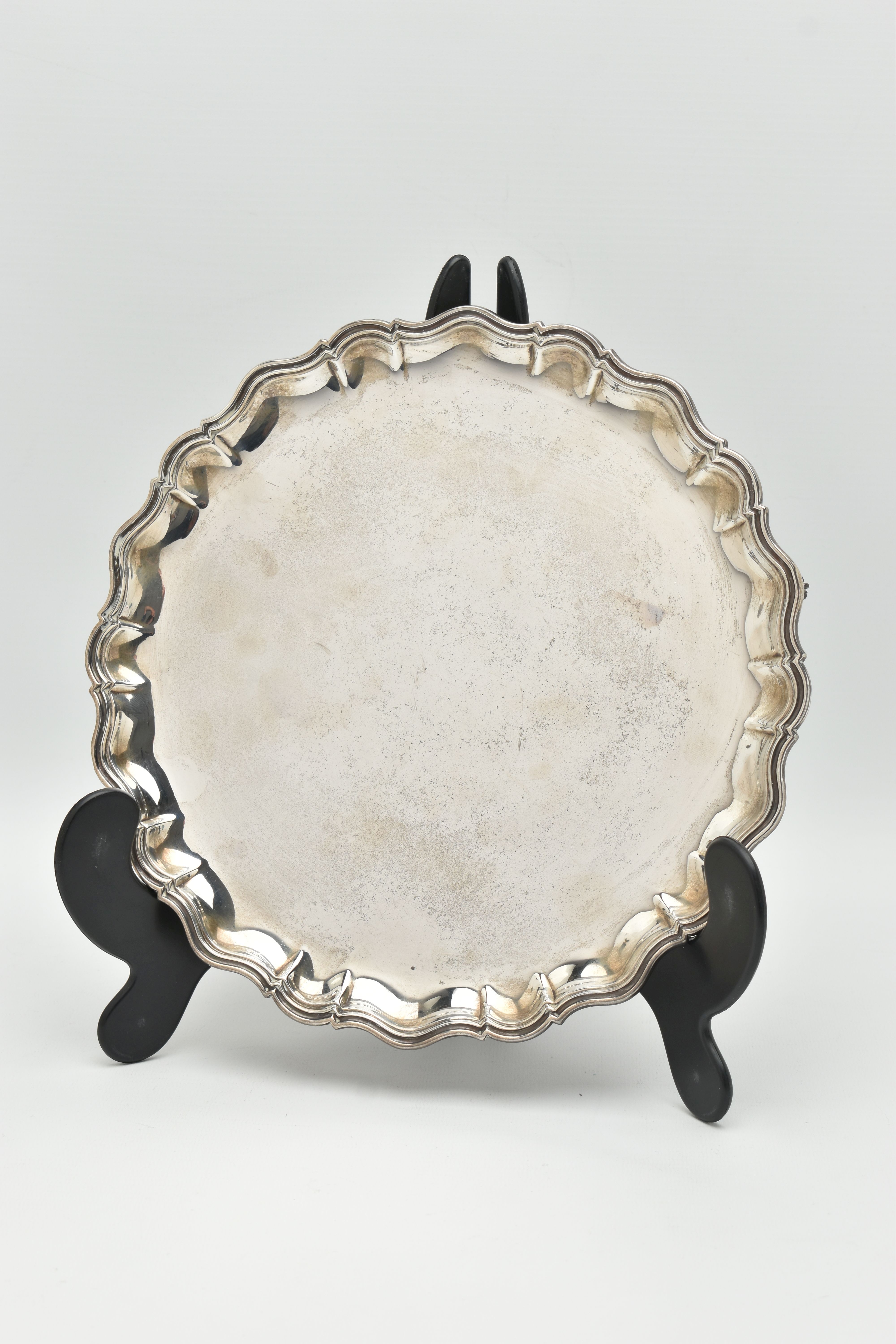 AN EDWARDIAN SILVER SALVER, polished round wavy form, raised on three scroll feet, hallmarked 'James