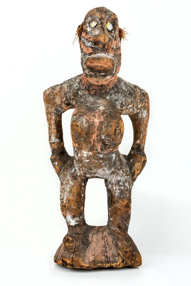 A tribal carved wooden figure of a woman, stood with bent knees and hands held on her hips, with red