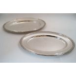 Two silver plated oval serving platters by Christofle, both with a ribbon and reed border, both