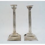 A pair of white metal Corinthian column candlesticks, the detachable sconces with gadrooned