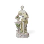 A Bow figure of Flora, emblematic of Spring, c.1758-60, modelled standing beside a vase encrusted...