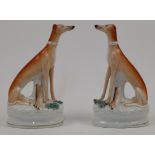 A pair of Staffordshire greyhounds, 19th century, with ochre backs, each modelled seated beside a...