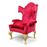 A wingback armchair, in the George I style, 20th century, upholstered in red velvet with embossed...
