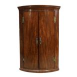 A George III mahogany bowfront hanging corner cupboard, c.1780, the moulded cornice above two doo...