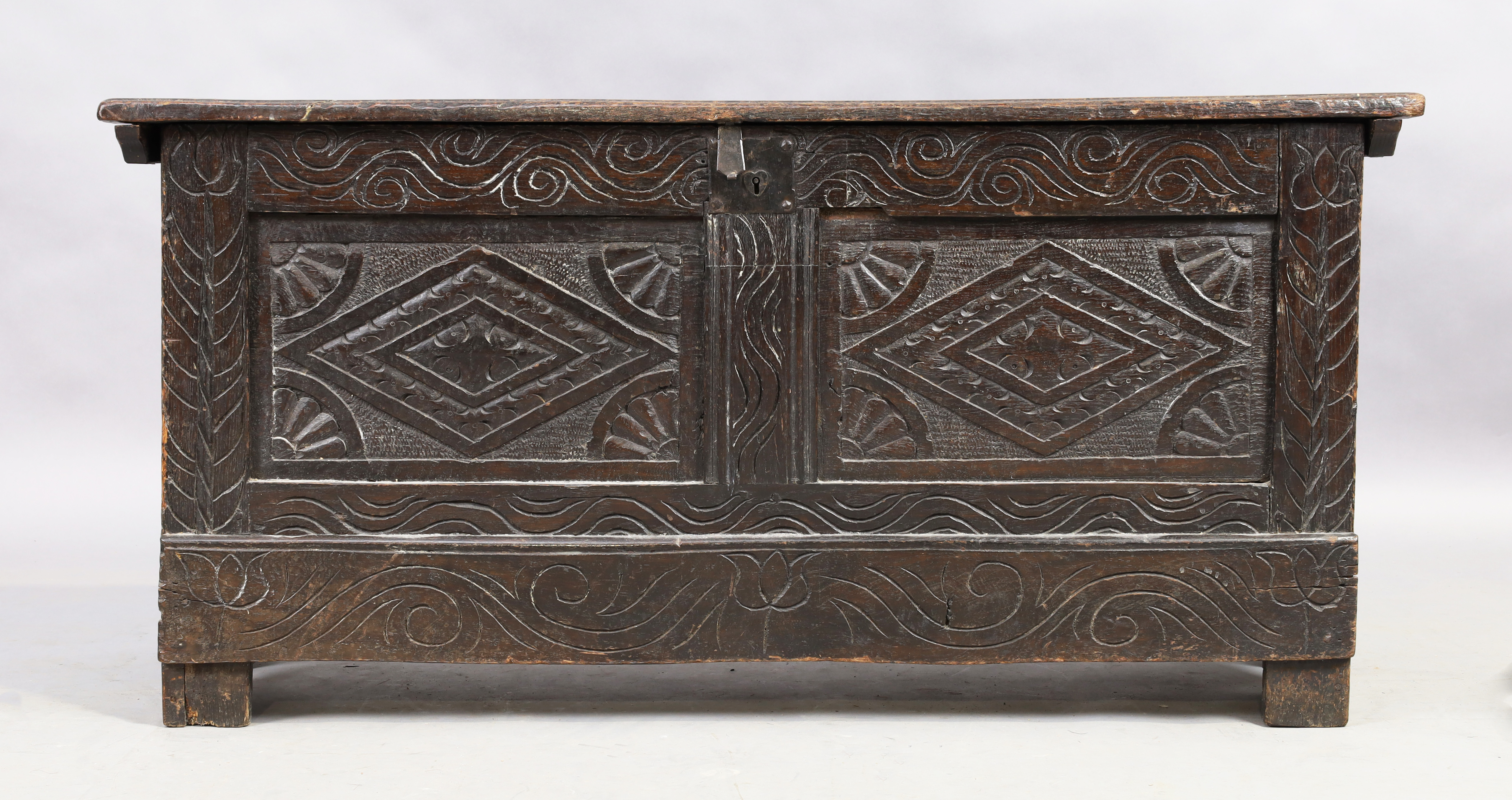 An English oak coffer, 18th century, floral carved, the hinged lid enclosing candle box and compa...