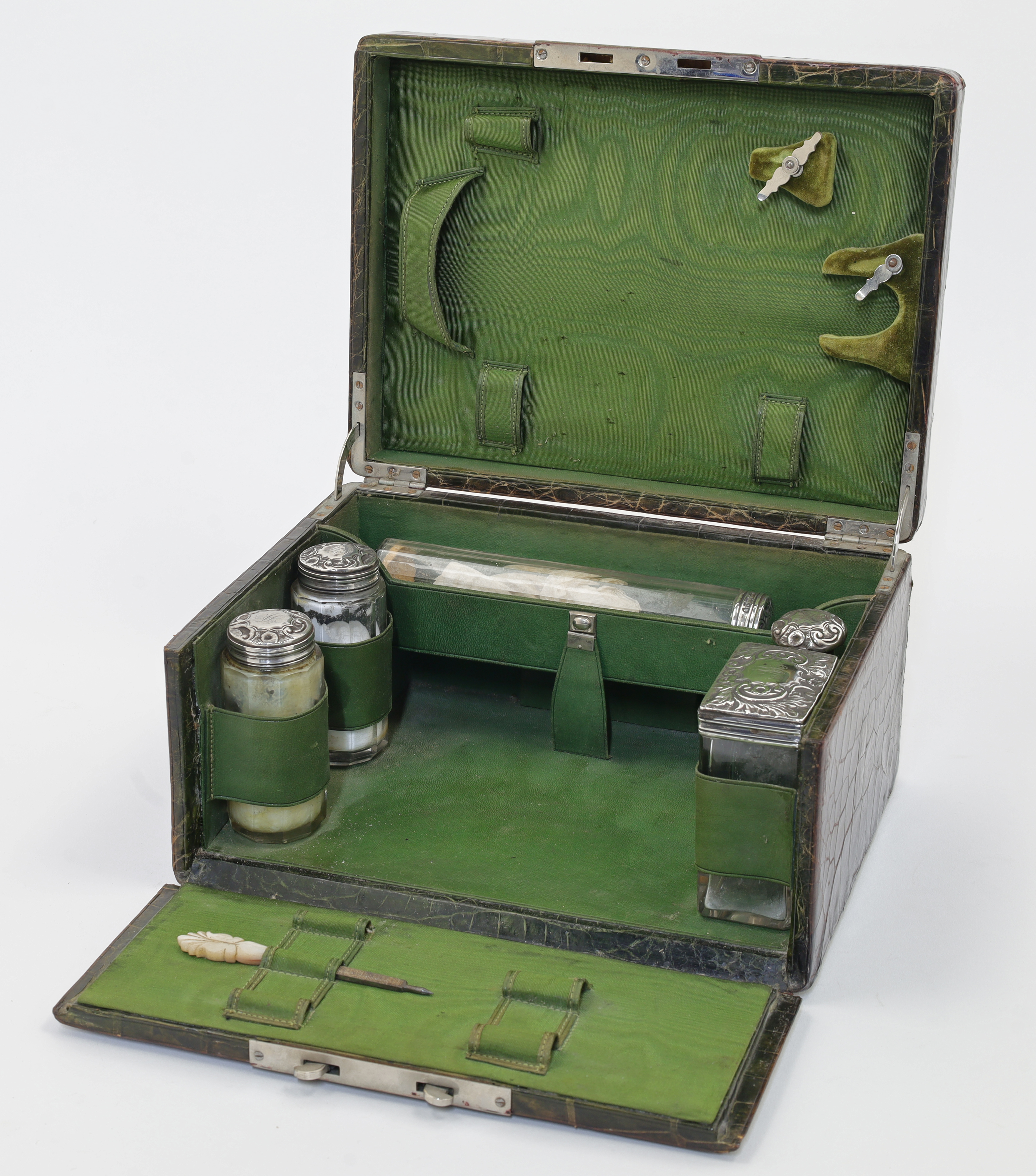 A crocodile skin travelling vanity case, enclosing a partially fitted interior with five silver t...