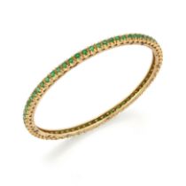 An emerald set bangle, with a continuous row of circular mixed-cut emeralds, claw set to plain gu...