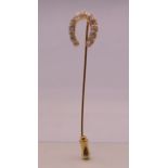 An unmarked gold diamond set horseshoe form stick pin. 6.5 cm long. 2.3 grammes total weight.
