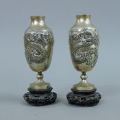 A pair of small Chinese silver vases, each mounted on a carved wooden stand. 14.5 cm high overall.