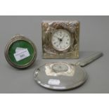 A silver hand mirror, a silver frame and a silver plated clock. The latter 11 cm high.