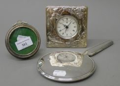 A silver hand mirror, a silver frame and a silver plated clock. The latter 11 cm high.