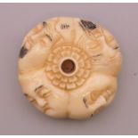 A bone netsuke carved with faces. 4 cm diameter.