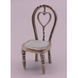 A silver miniature model of a chair. 4.5 cm high.