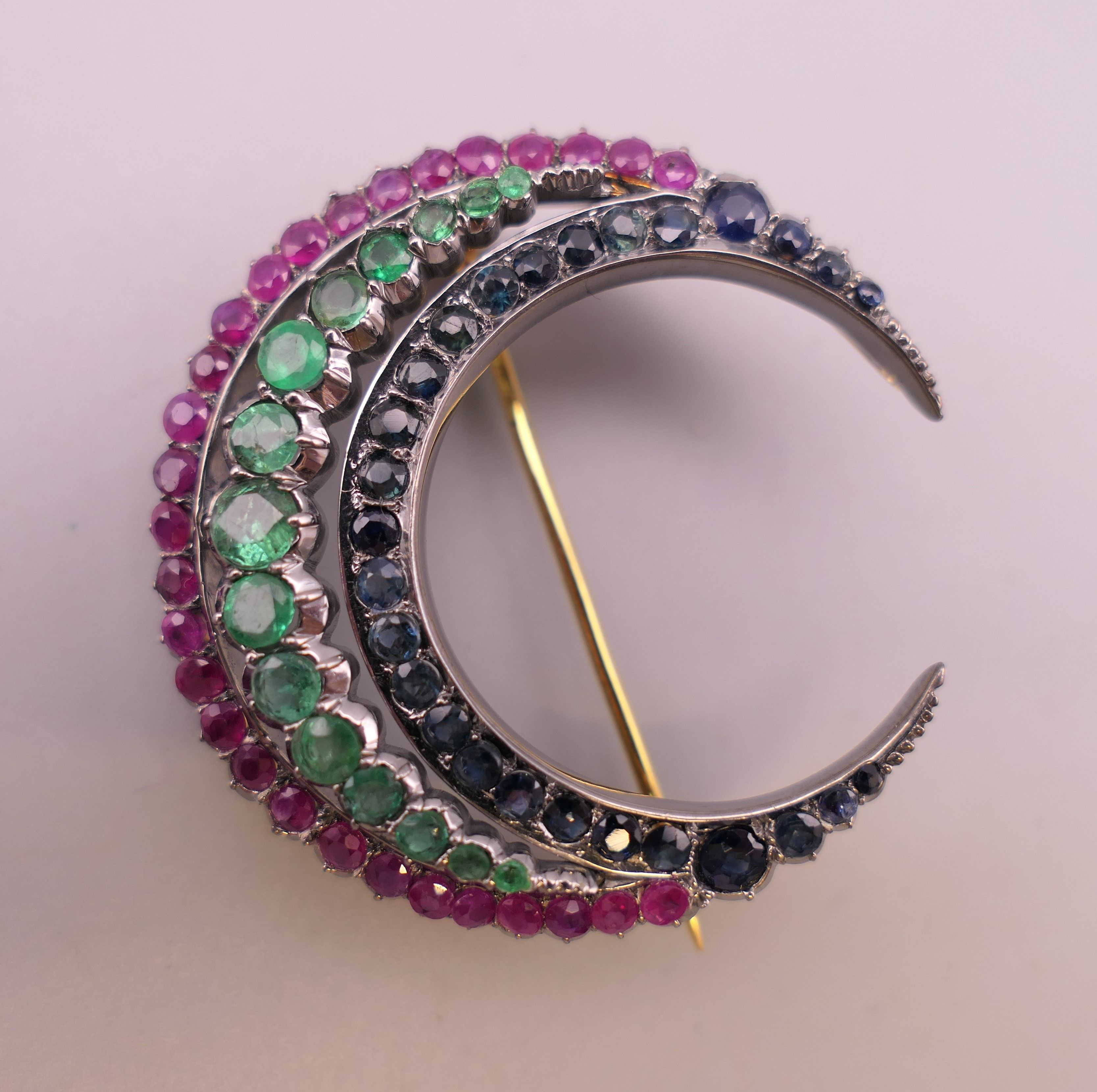 A silver and gold, ruby, emerald and sapphire crescent form brooch. 4 cm wide.