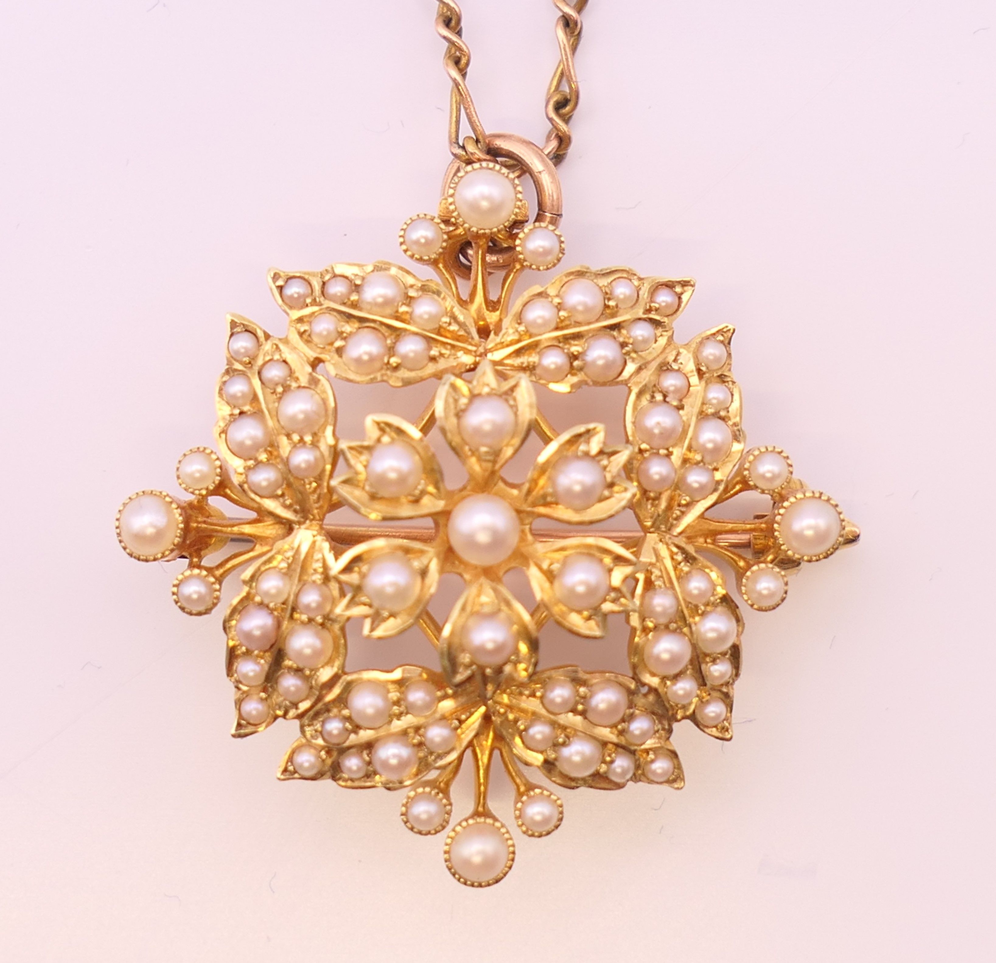 A 15 ct gold and seed pearl pendant/brooch on a 9 ct gold chain.