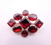 An early Victorian unmarked gold and garnet brooch, cased. 3 x 2 cm. 2.3 grammes total weight.