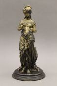 An antique sculpture in art metal of a Grecian maiden standing in front of a stool,