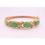 An 18 ct gold apple green faceted jade and diamond bangle form bracelet. 5 cm internal diameter.