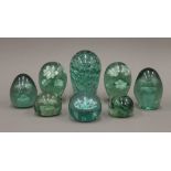 A collection of eight green glass dump weights. The largest 15 cm high.